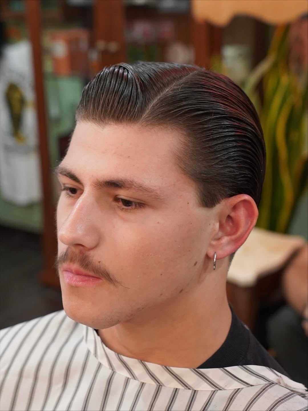 slicked 1940s comb over haircut with a defined side part and high-shine pomade finish