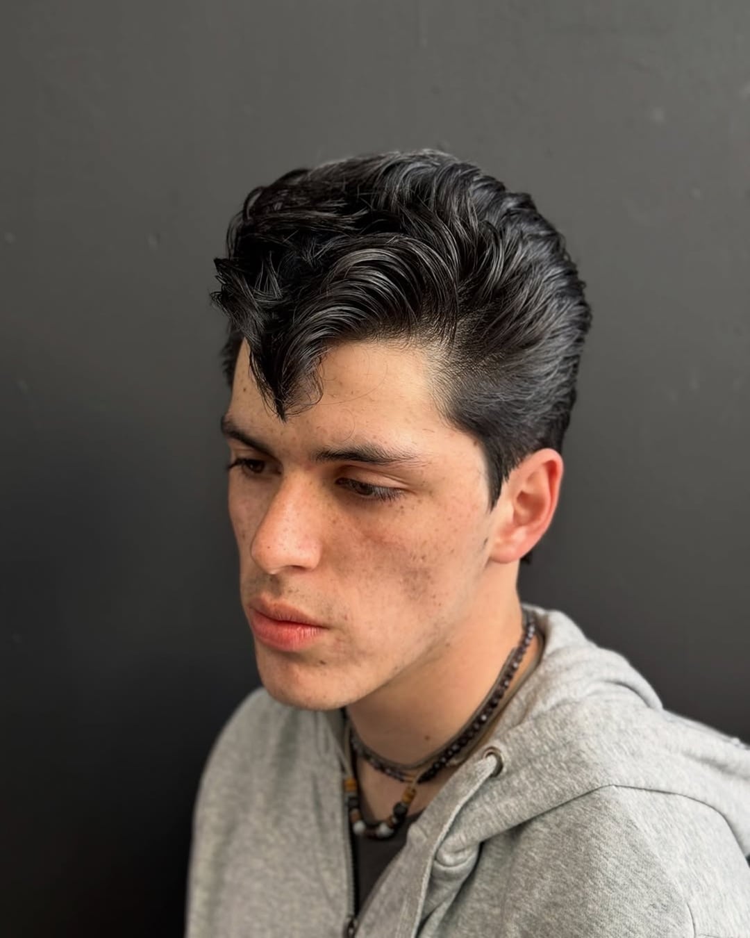 dark 1950s greaser-style pompadour with a high-volume wavy top and a distinct forward-curved front quiff