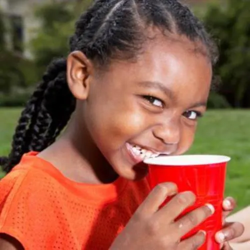 Girl (5-7) drinking from disposable cup, smiling, portrait