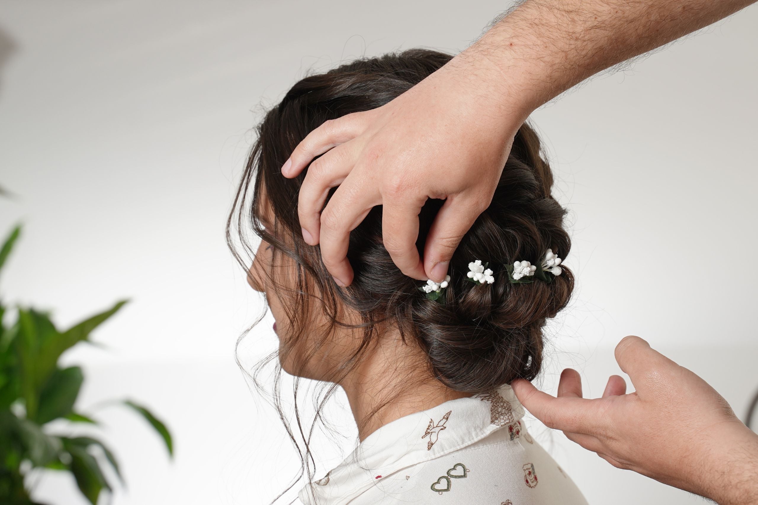 Stylist adding baby&rsquo;s breath flowers to the soft low bun with a reverse fishtail braid and flat twist.
