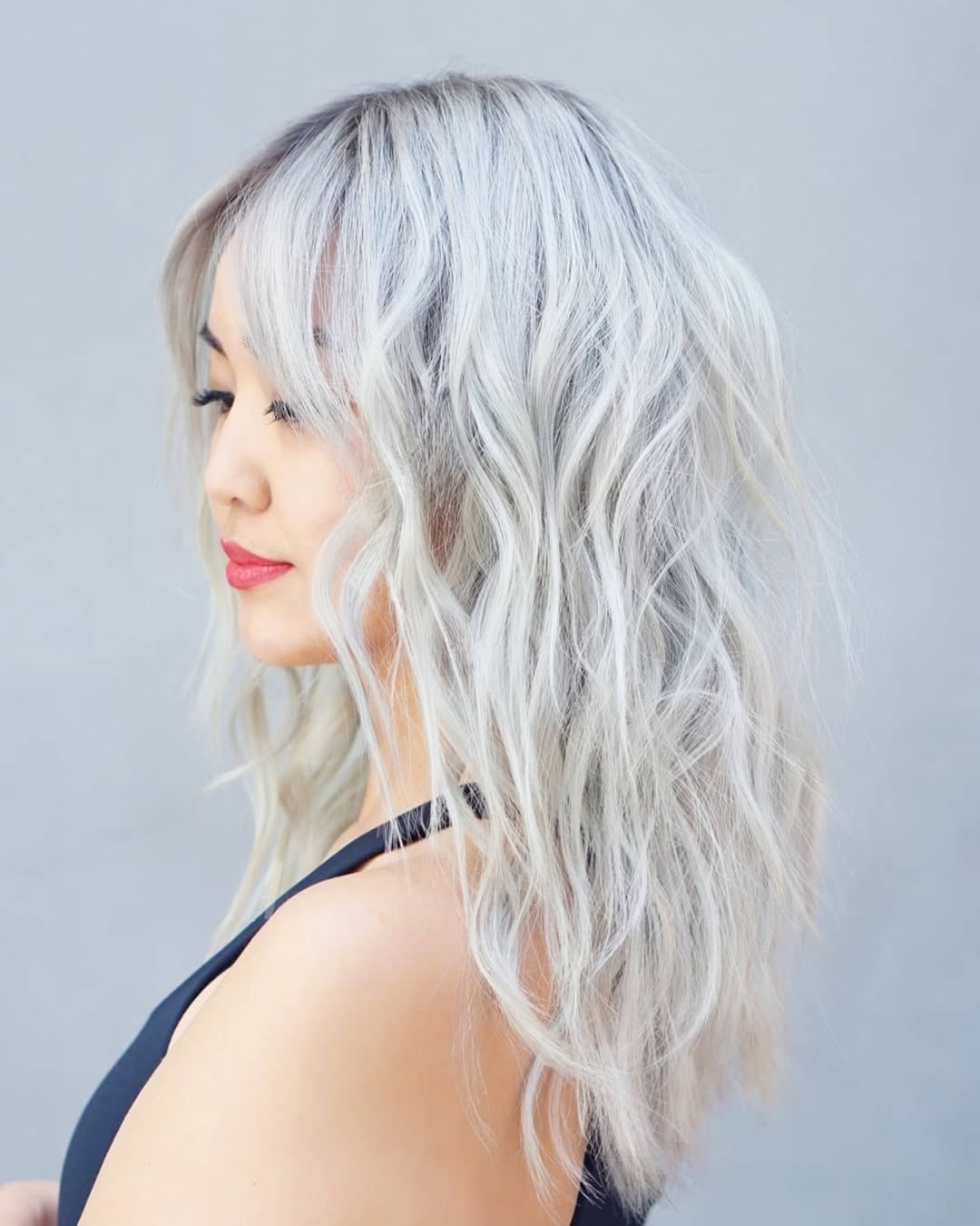 Asian woman with wavy silver blonde lob and curtain bangs