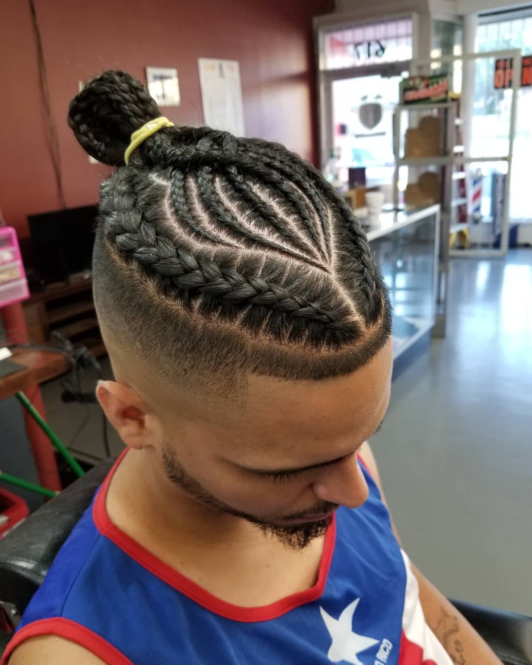 Puerto Rican man displaying a braided top knot haircut with a sharp lineup fade