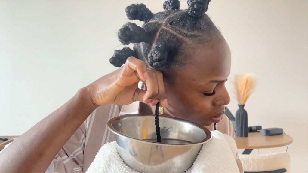 The stylist dips the coiled side braid end into hot water while holding a towel under the bowl.