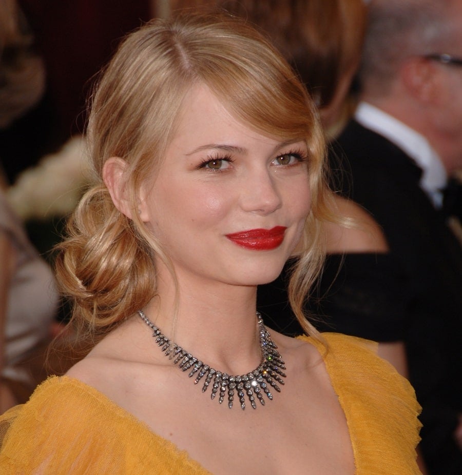 Michelle Williams blonde hair styled in a low side messy bun and soft side-swept bangs