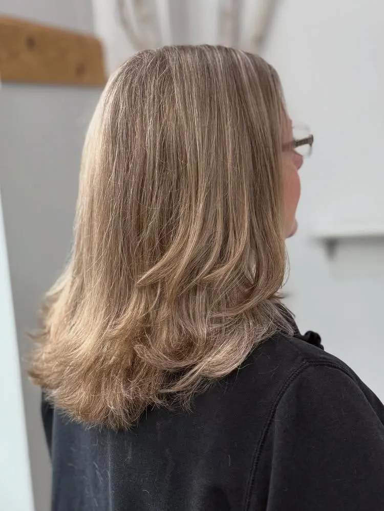 Back view of an older woman with medium length ash blonde hair featuring soft, flipped-out layered ends.