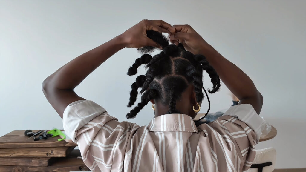 Back view of curved hair sections tied at the roots and twisted before braiding.