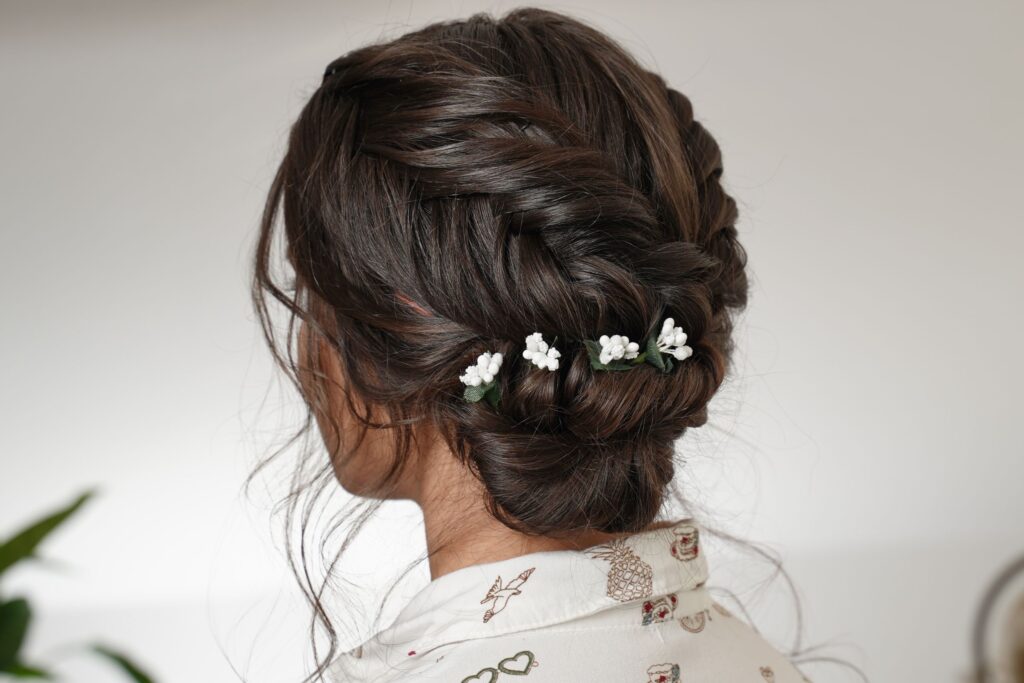 Back view of a reverse fishtail braid and flat twist floral low bun updo finished with baby&rsquo;s breath flowers.