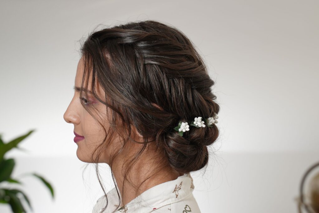 Side view of the reverse fishtail braid and flat twist low bun updo with baby&rsquo;s breath flowers and soft face-framing curls.