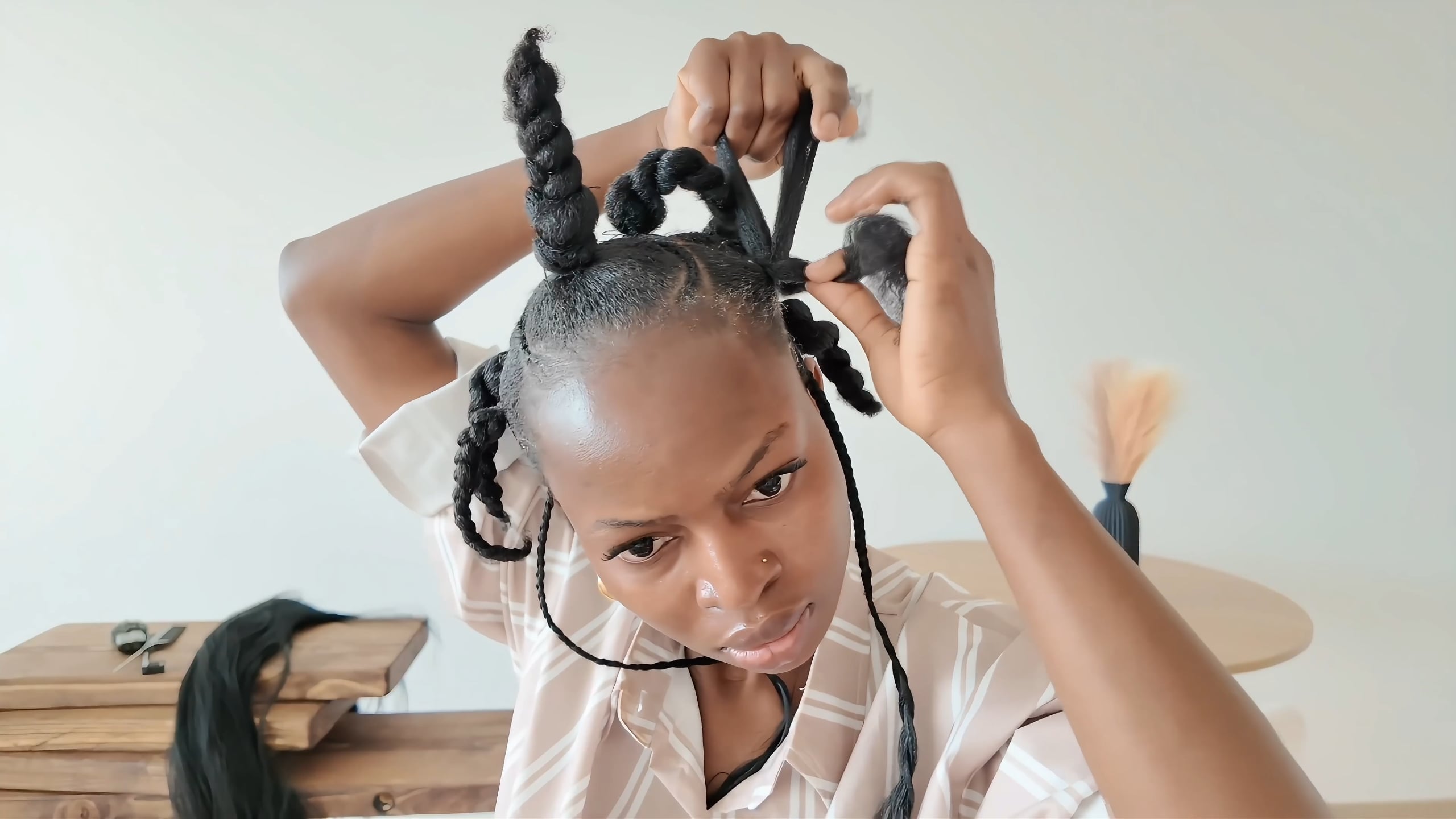 The stylist untwists a tied section and begins braiding before feeding in extension.