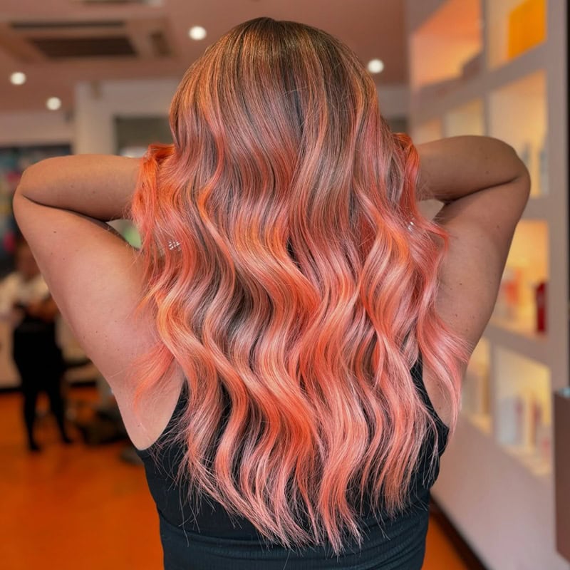 long, wavy hair dyed in vibrant peach and coral gradient.