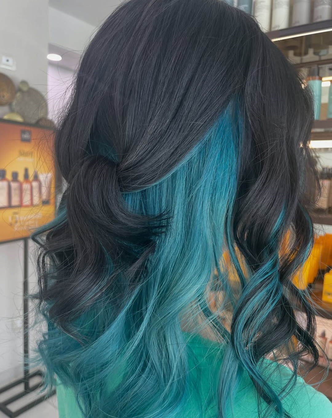 Dark black hair with bright teal hidden hair colors styled in half-up loose waves