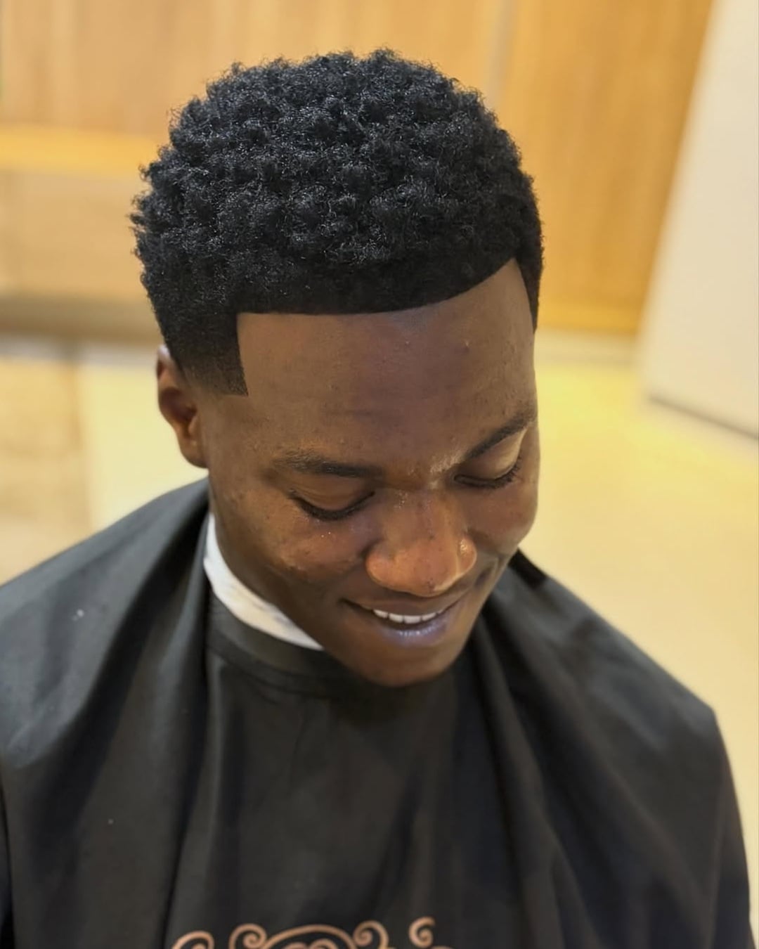 short textured black afro curls with a low taper fade and sharp lineup