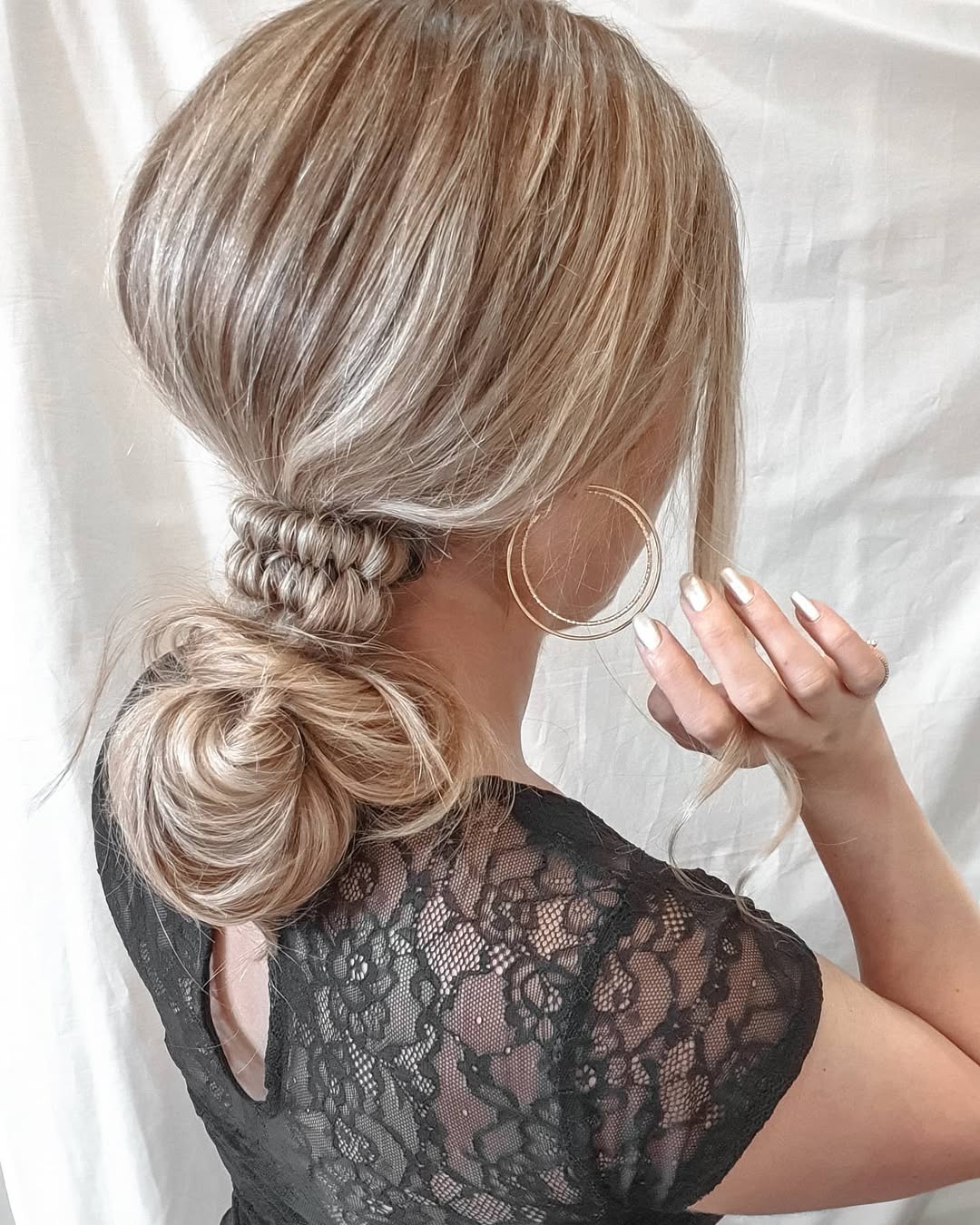 Back view of a woman featuring a sandy blonde low messy bun accented by an intricately woven base wrap
