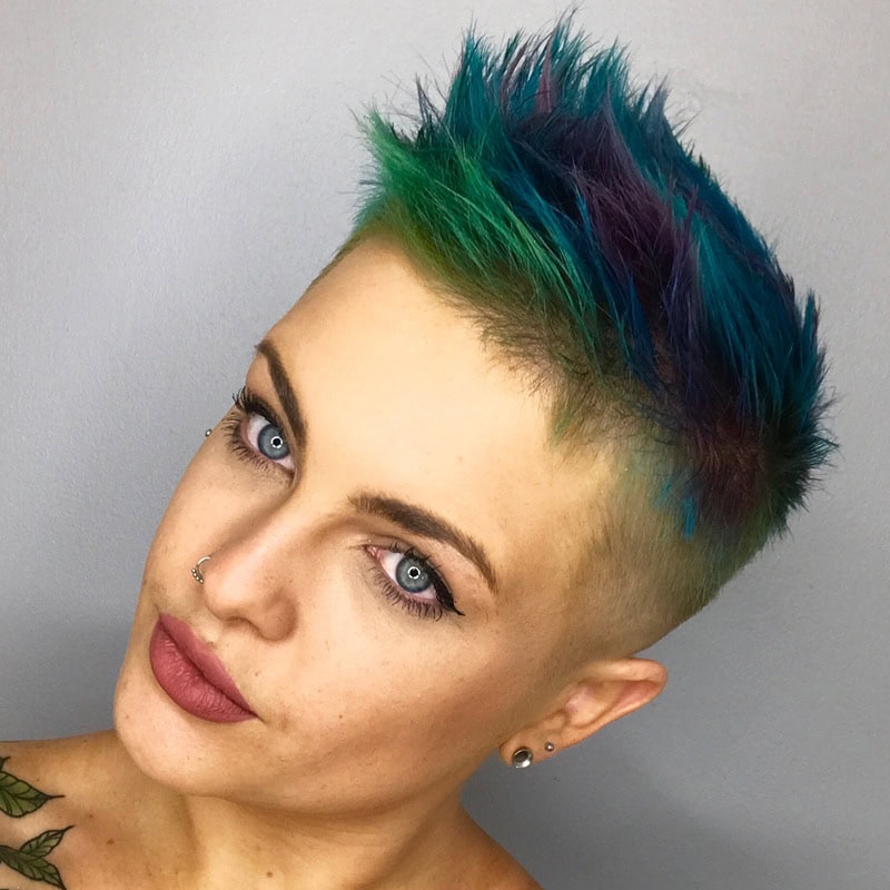 Short spiky blue and green pixie cut with shaved sides and violet accents