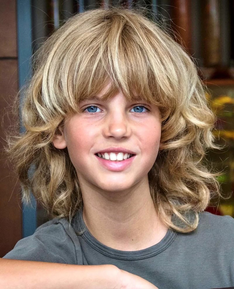 young boy with wavy shoulder-length blonde hair and thick full bangs