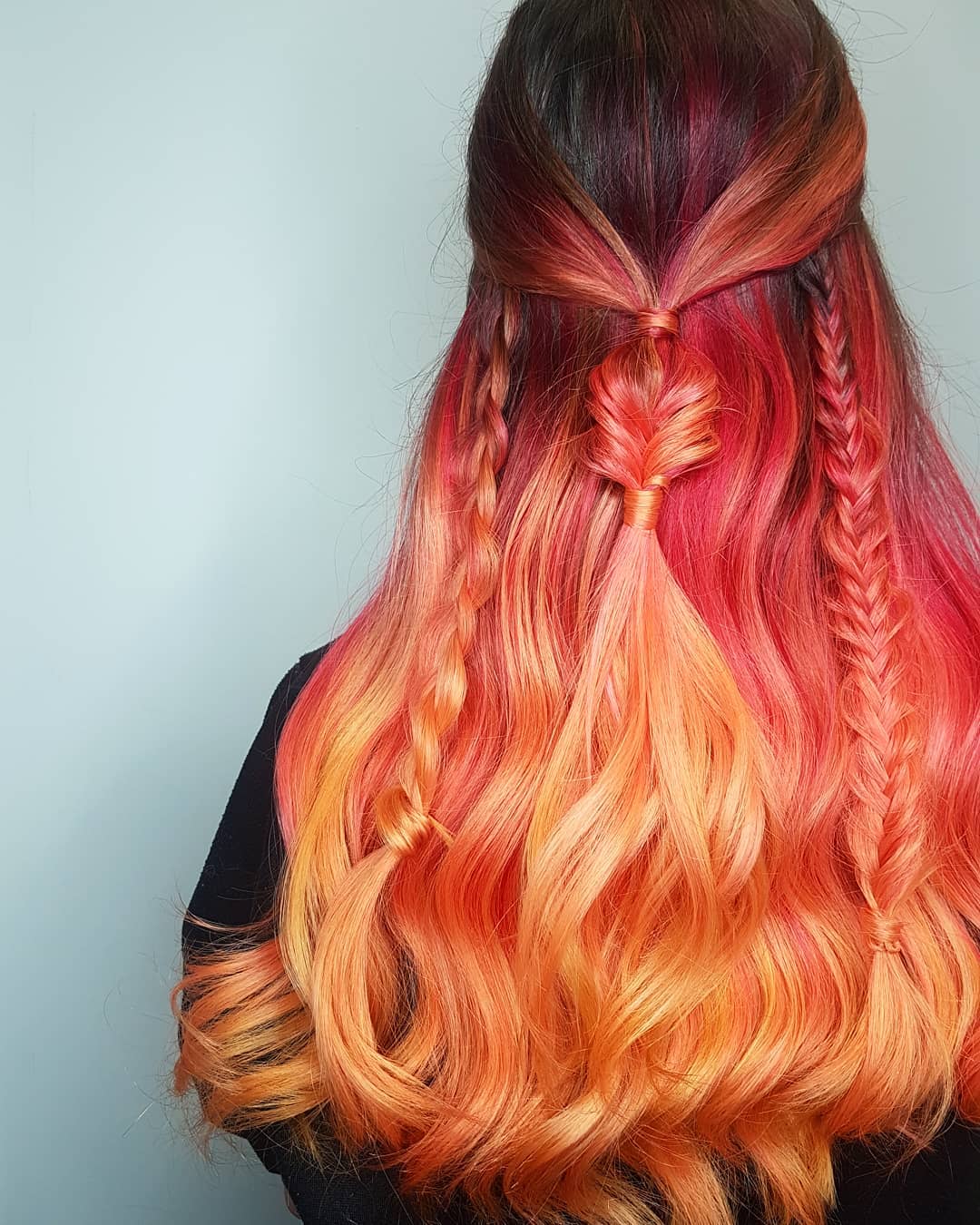 Long wavy hair with accent braids featuring a coral pink and orange ombre blend