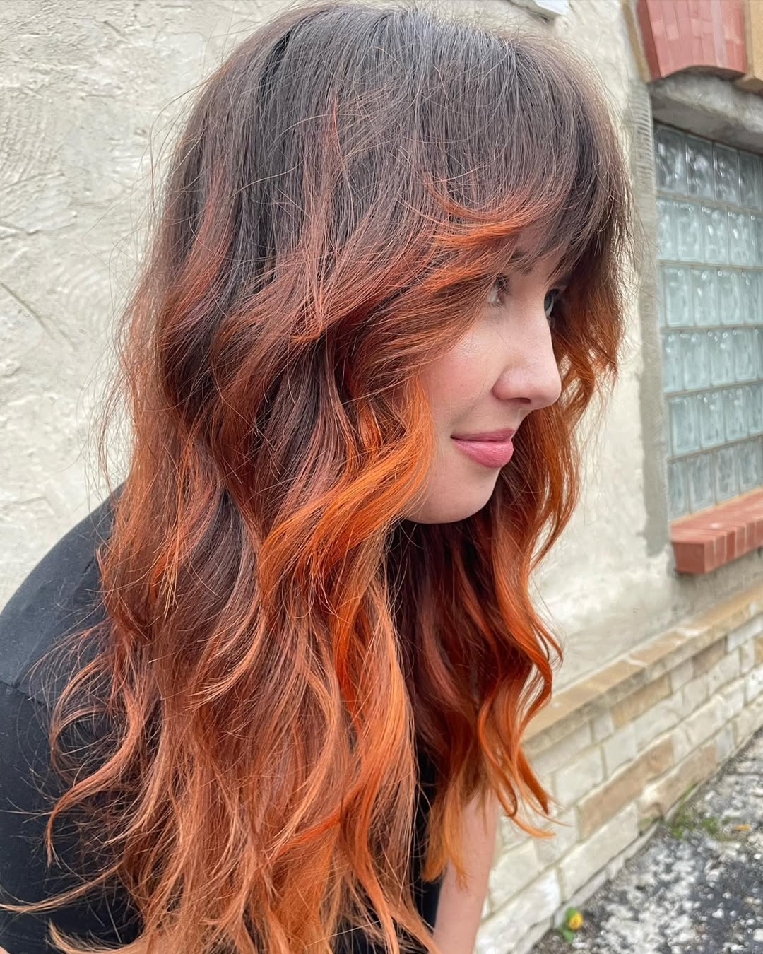Long wavy shag with curtain bangs styled in a bronze orange ombre