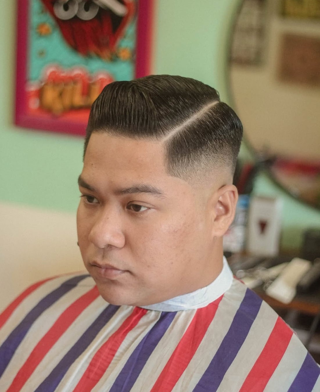 Man with a slick pompadour comb over haircut featuring a sharp hard side part and a clean mid fade