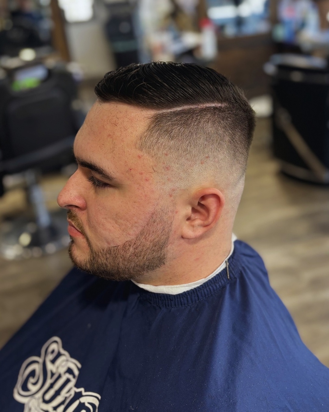 Man with a mid skin fade, clean side part, and neatly combed over section