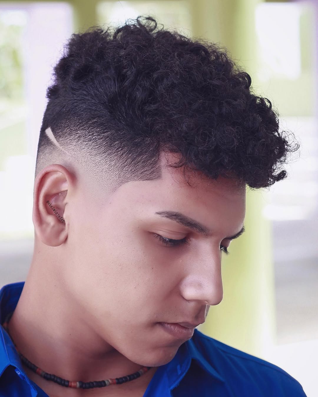 Man with a curly skin fade comb over, sharp line-up, and shaved hair-slash side accent