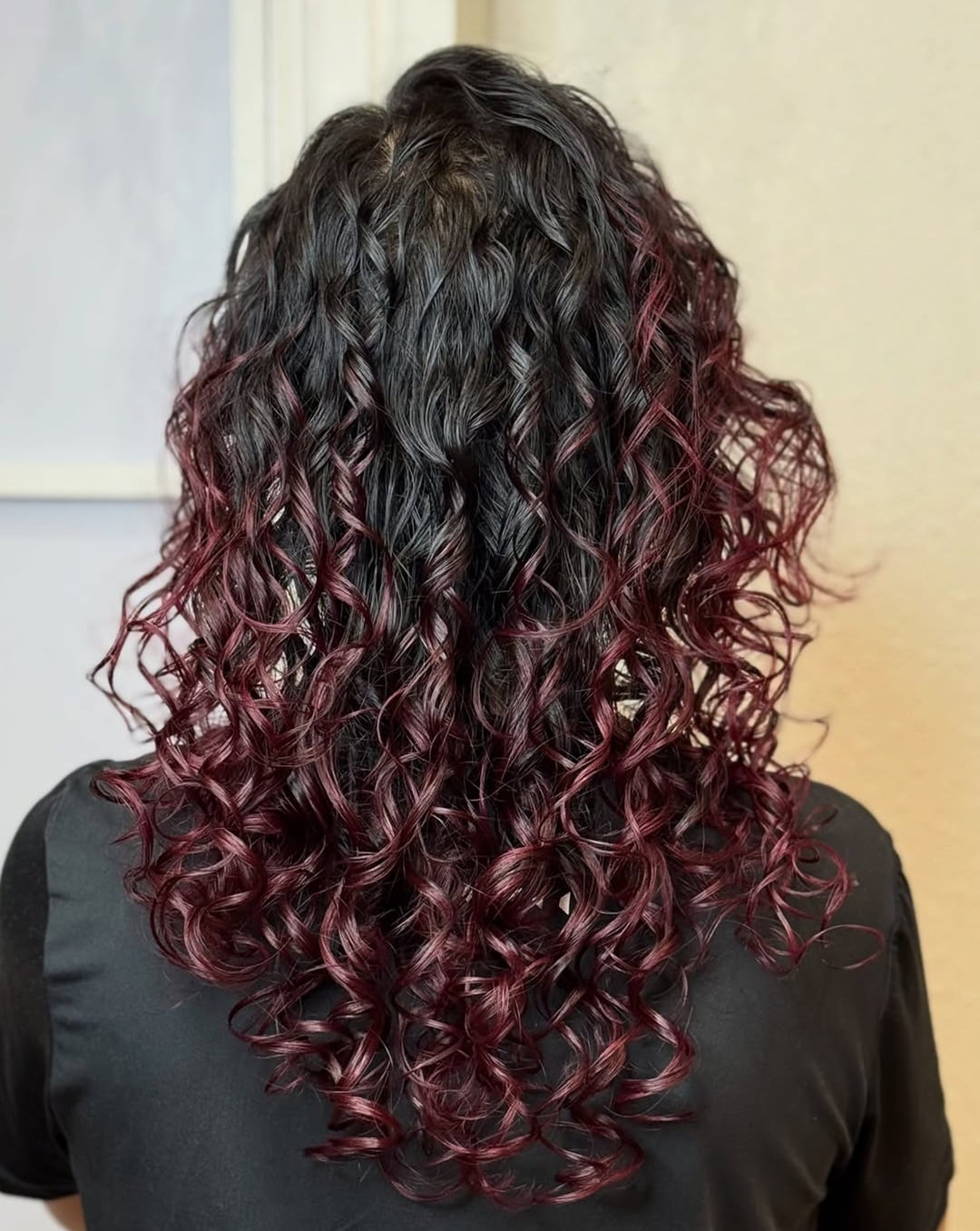 Back view of long curly hair with dark red wine balayage highlights