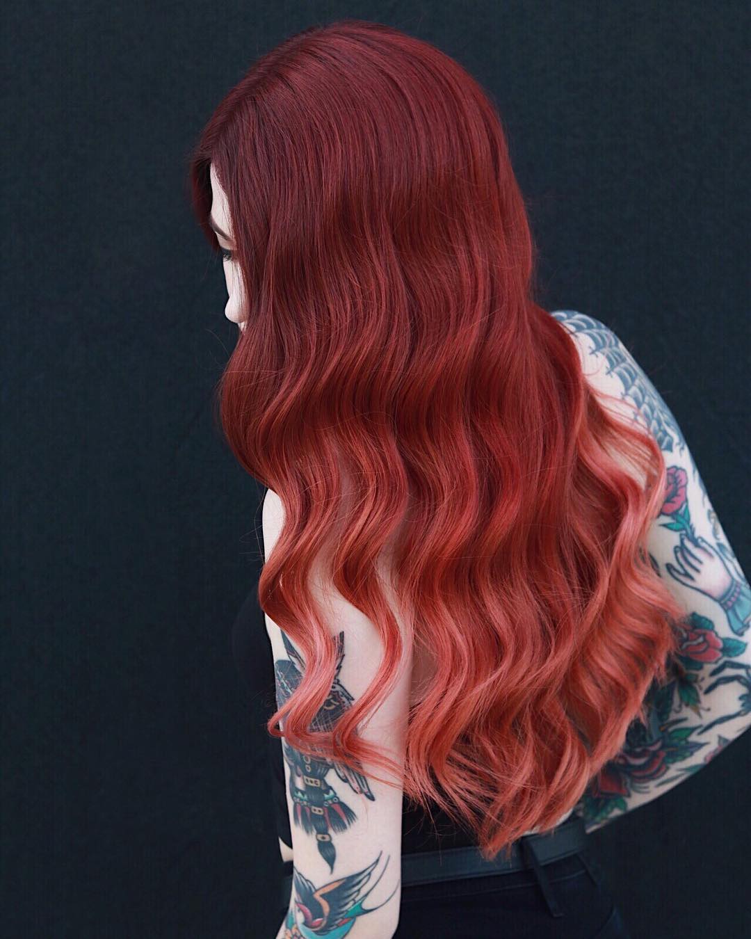Long wavy hair with a deep red base blending into a peachy rose gold ombre hair color