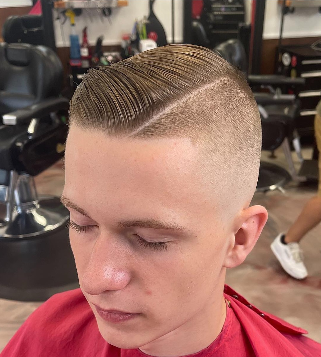Young man with a high skin fade, razor hard part, and slick disconnected comb over