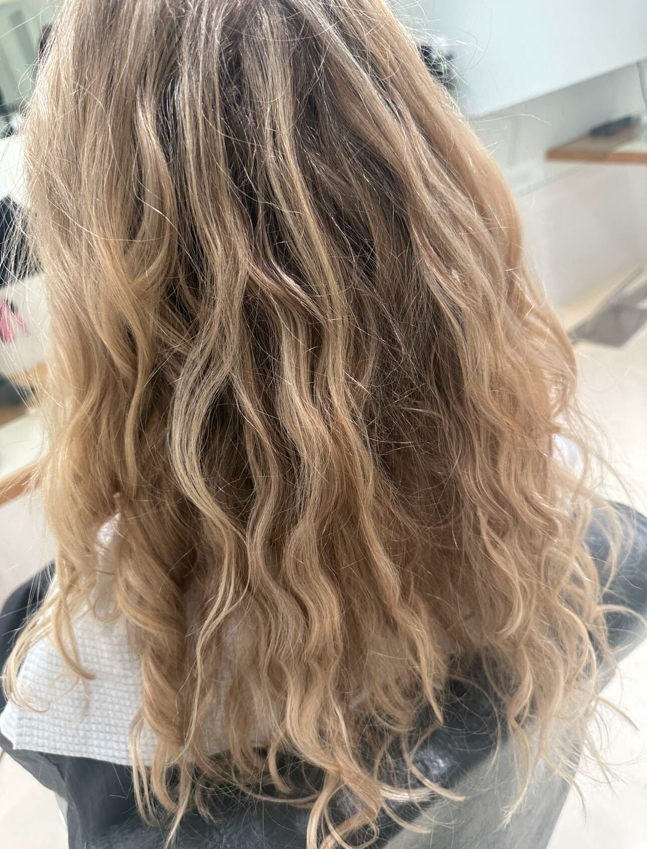Back view of long wavy blonde hair worn dry and unstyled in the salon chair, showing its natural texture