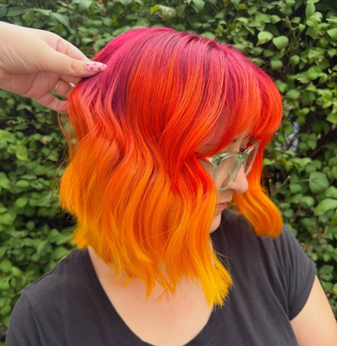 Short wavy bob with bangs showcasing a fiery pink and orange ombre