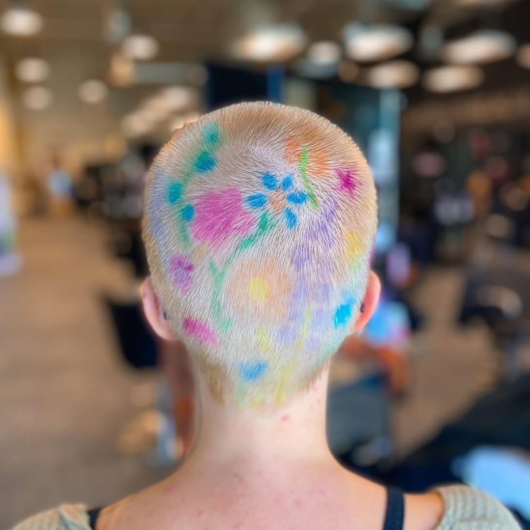 Blonde buzz cut for women styled with colorful hand-painted floral designs across the scalp