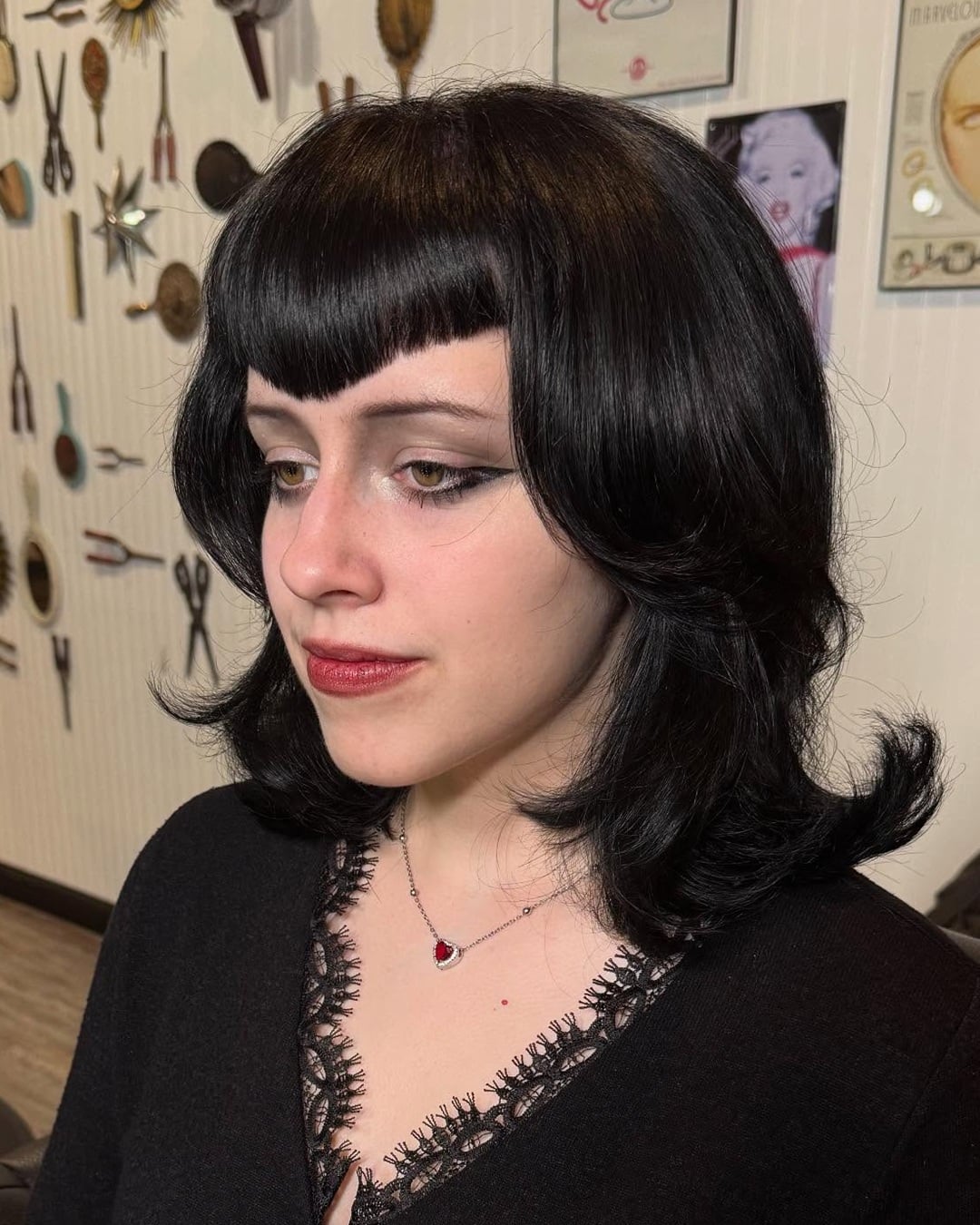 Jet black shoulder-length hair with triangle bangs and flipped ends styled in a gothic hairstyle