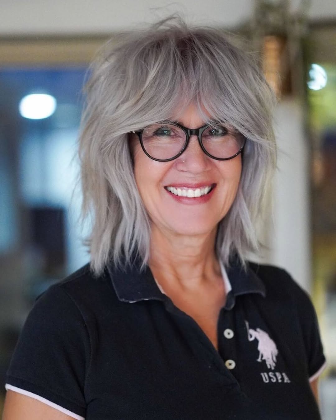 Older woman with a silver-gray shaggy bob, curtain bangs and glasses
