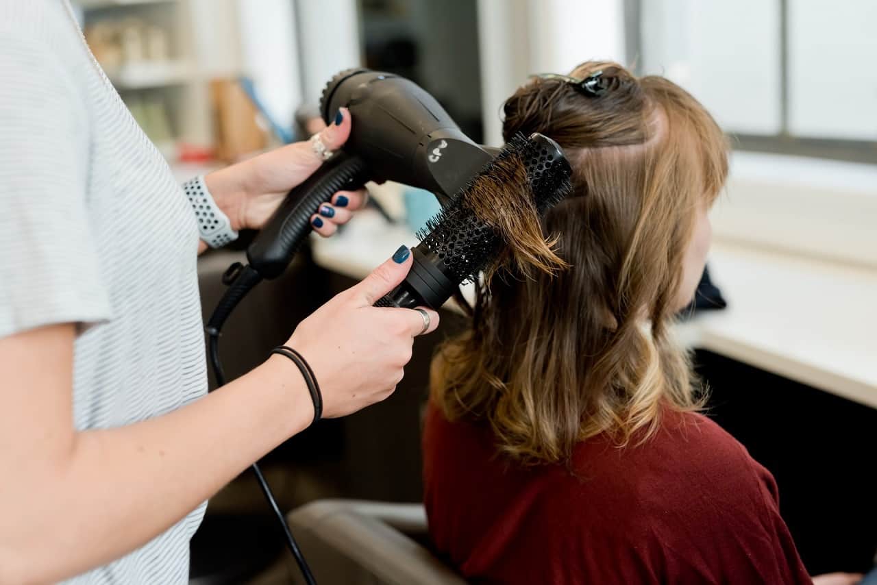 hair stylist drying hairs in salon with hair dryer