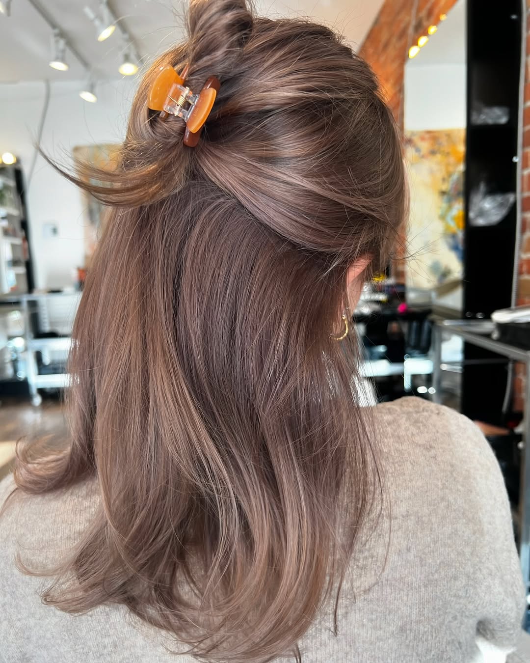 Woman with medium ash mousy brown hair styled in a half-up claw clip