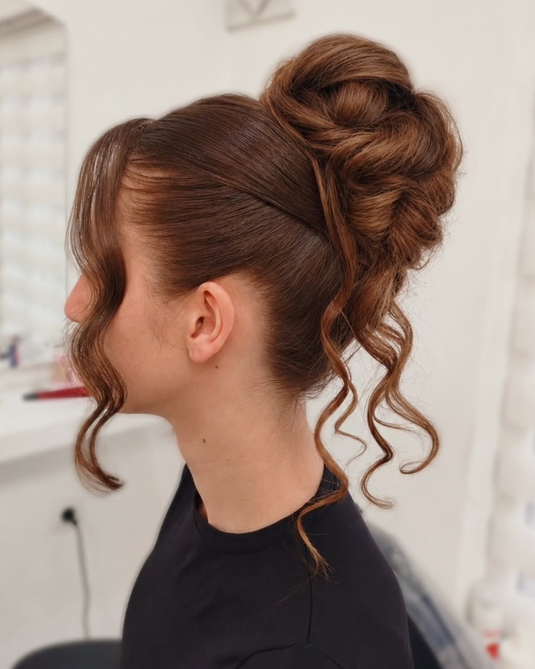 oman with long brown hair styled in a high voluminous updo bun with curly tendrils.