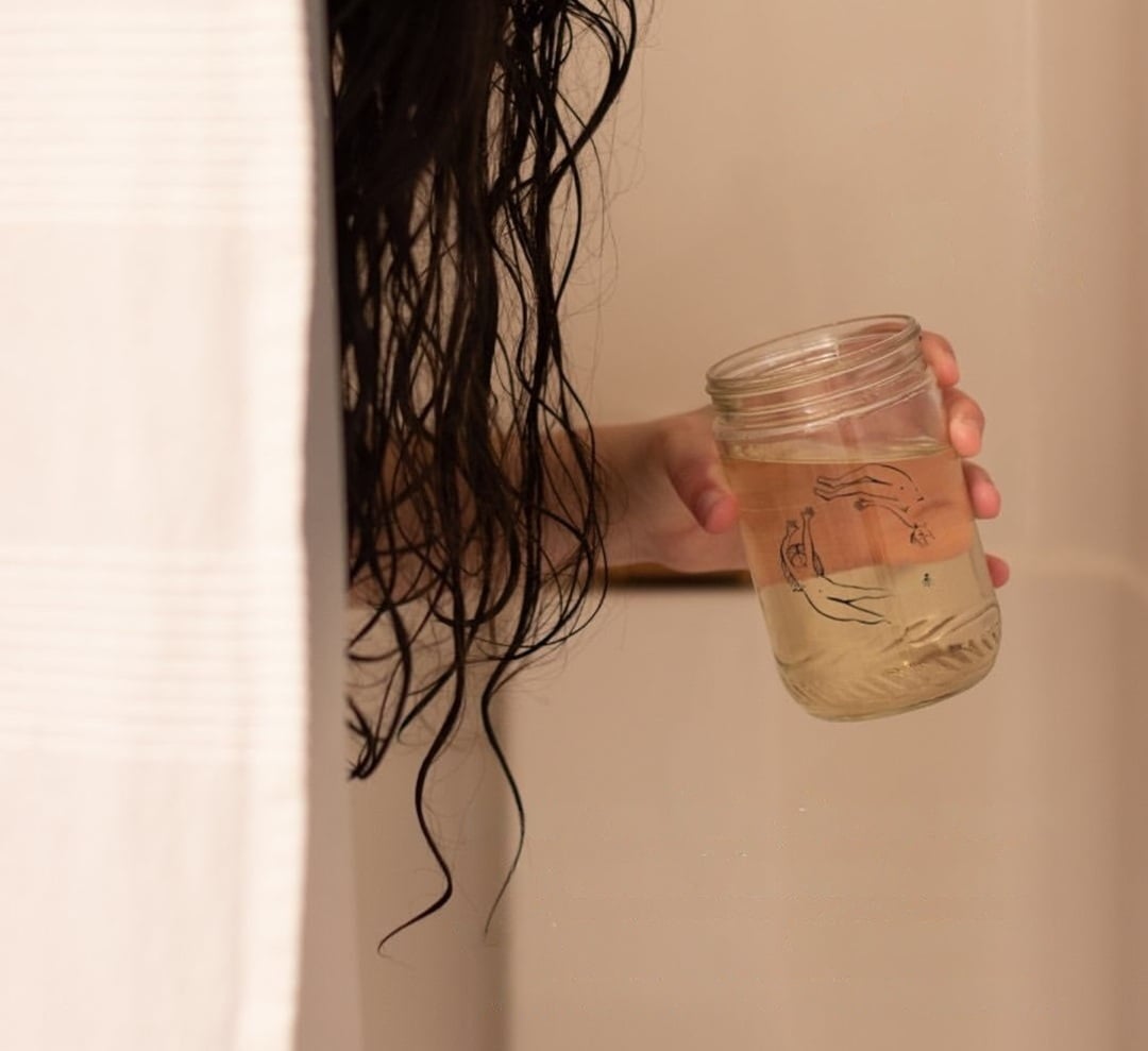 Glass jar of diluted apple cider vinegar hair rinse held in the shower for a natural hair moisturizing routine