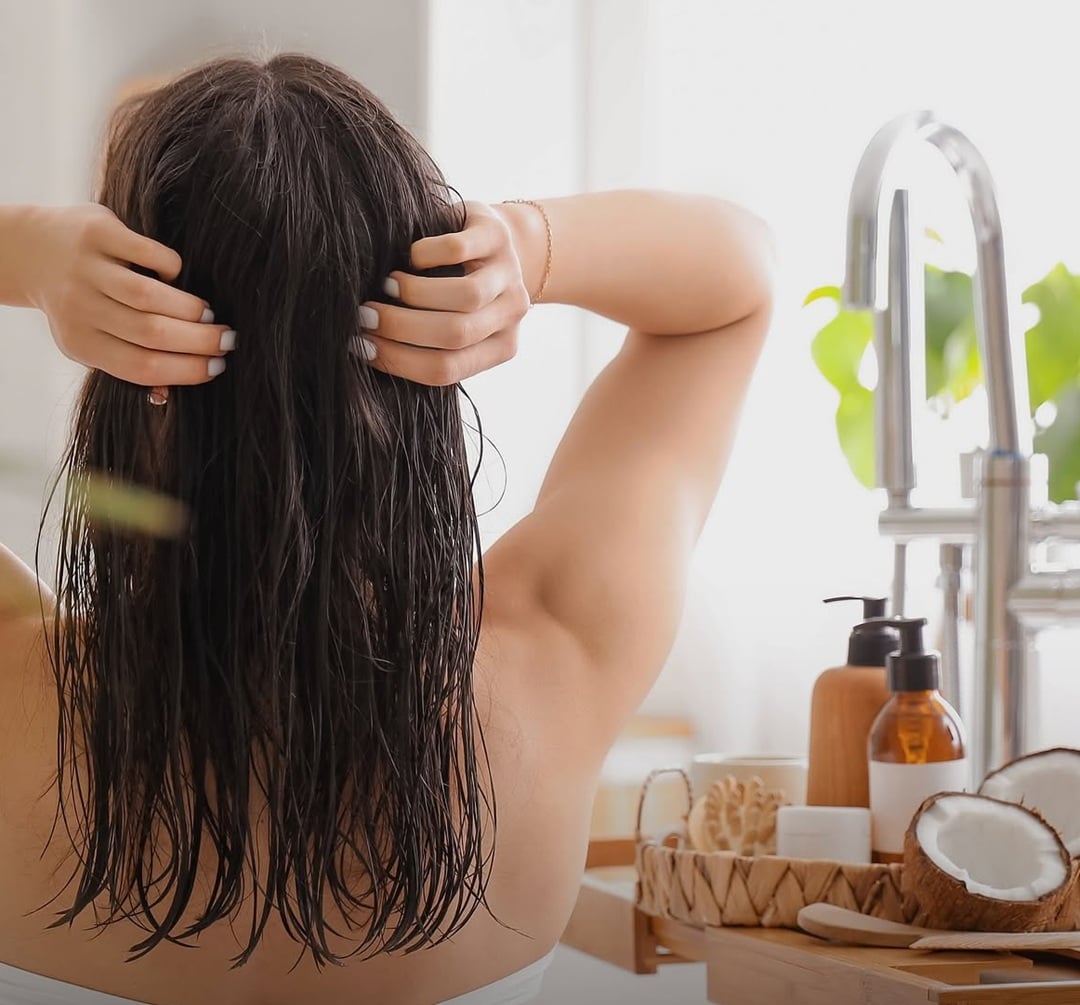Woman massaging warm coconut oil into damp hair for a homemade natural hair moisturizer recipe
