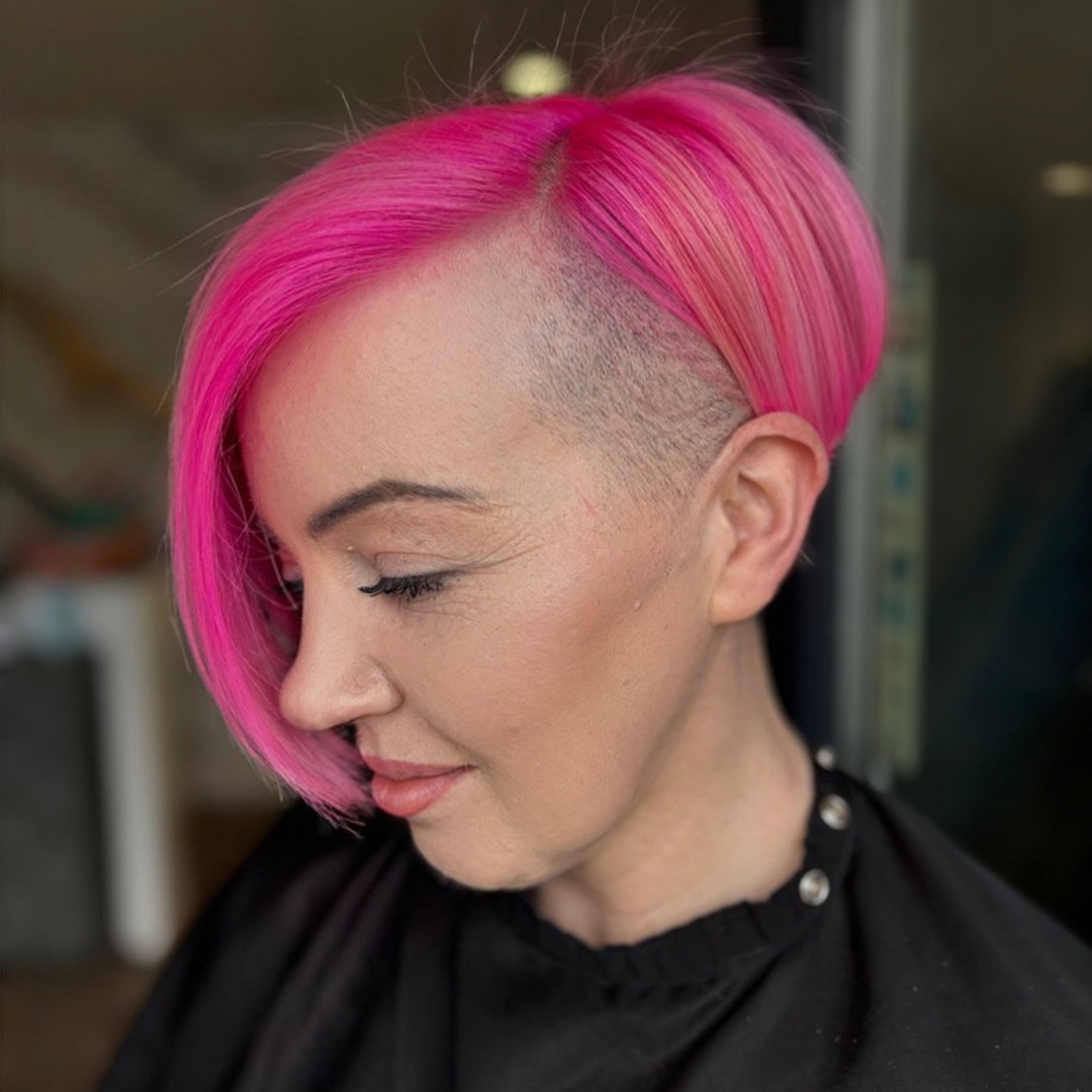 Woman with a straight hot pink asymmetrical undercut bob featuring a shaved side