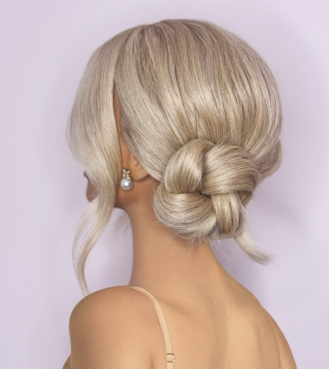 Ash blonde low knotted side bun updo with a loose face-framing tendril