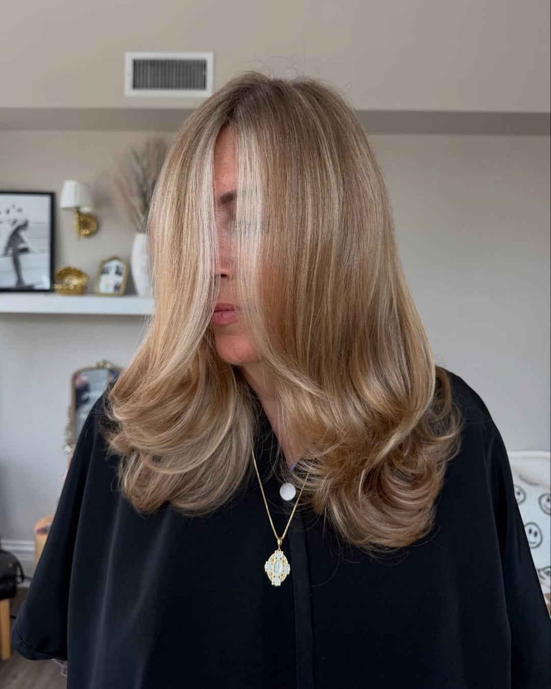 Woman with a bouncy layered blowout showcasing chestnut blonde balayage and face-framing highlights