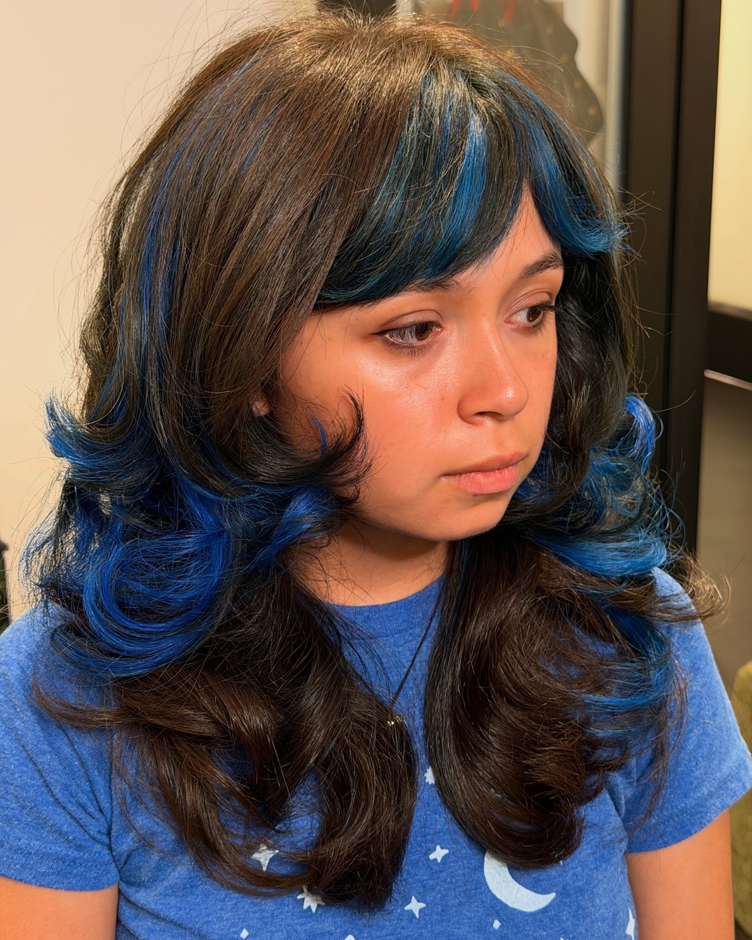 Woman with dark brown layered hair featuring electric blue highlights and voluminous side-swept bangs