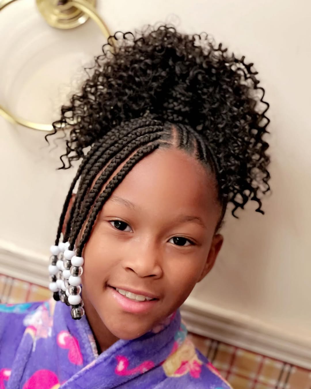 Little black girl styled in a high curly ponytail puff with cornrows and beaded side braids