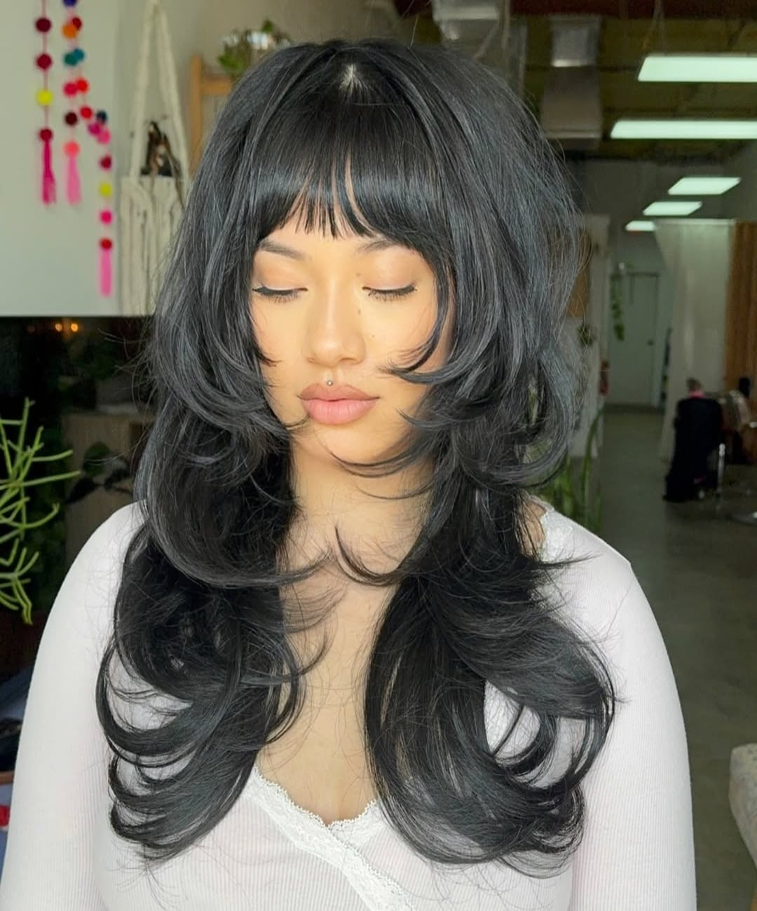 long dark hair featuring short face-framing layers, full bangs, and high-volume texture