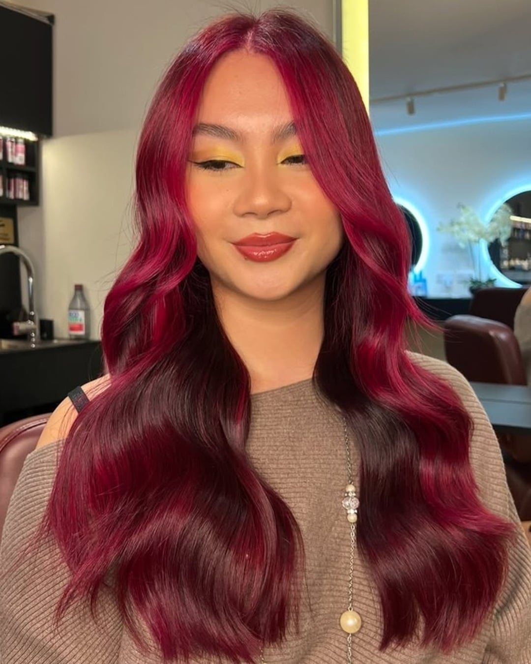 Woman with long center-parted red wine hair styled in smooth waves and face framing highlights
