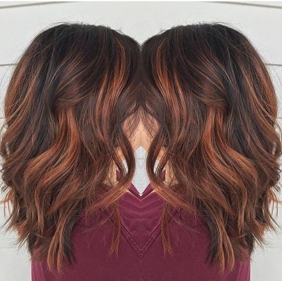 Long wavy dark brown hair enhanced with warm auburn and copper highlights