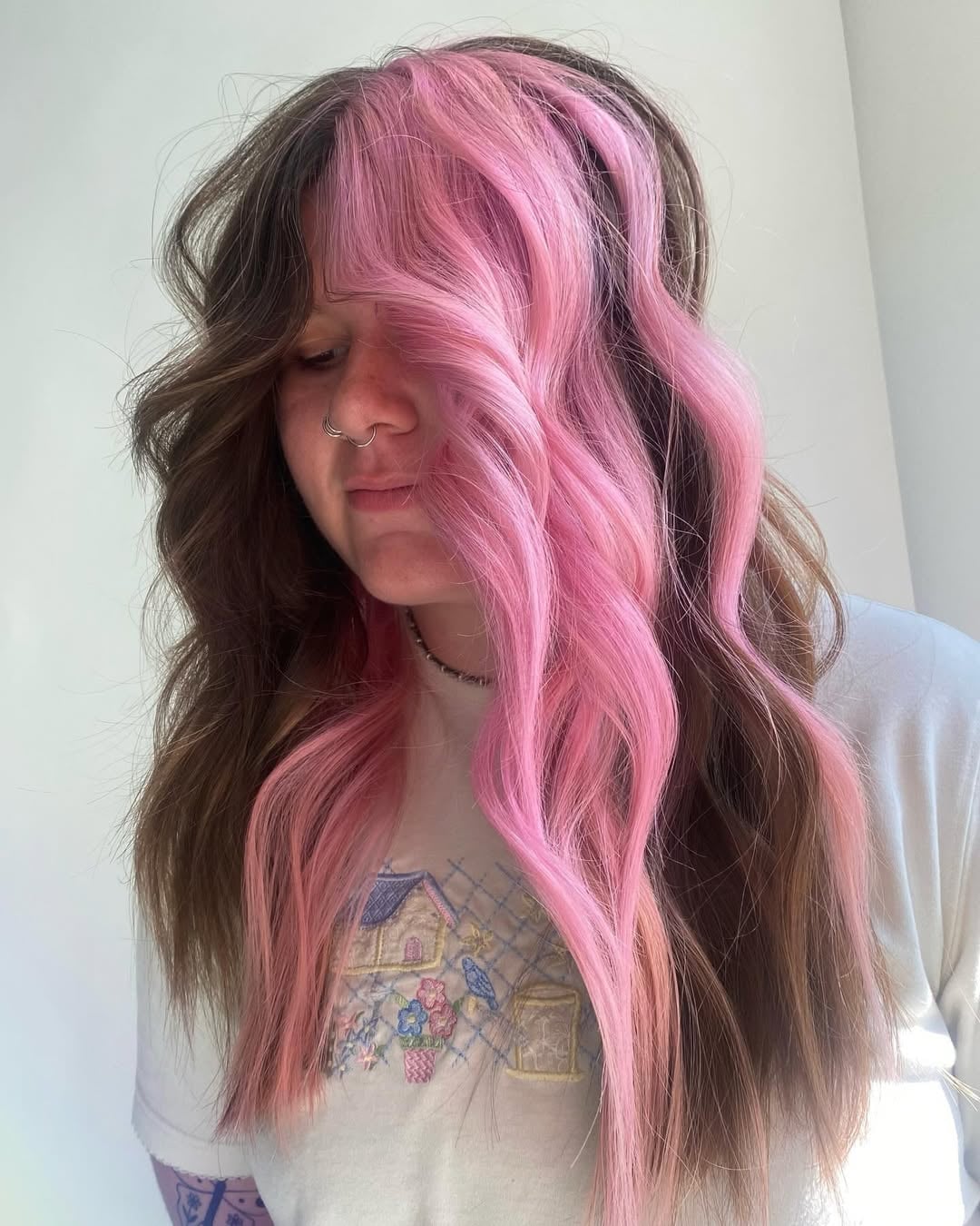 Woman with long wavy brunette hair featuring a bold pastel pink face-framing money piece