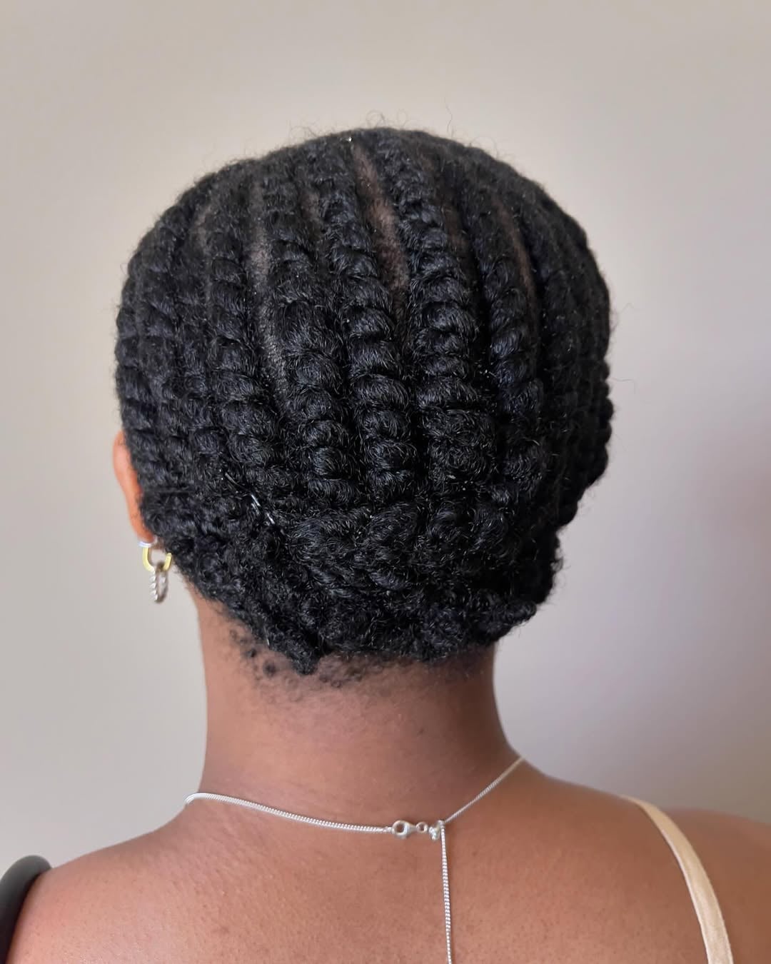 Black woman with neat vertical flat twists gathered into a low tucked bun updo at the nape