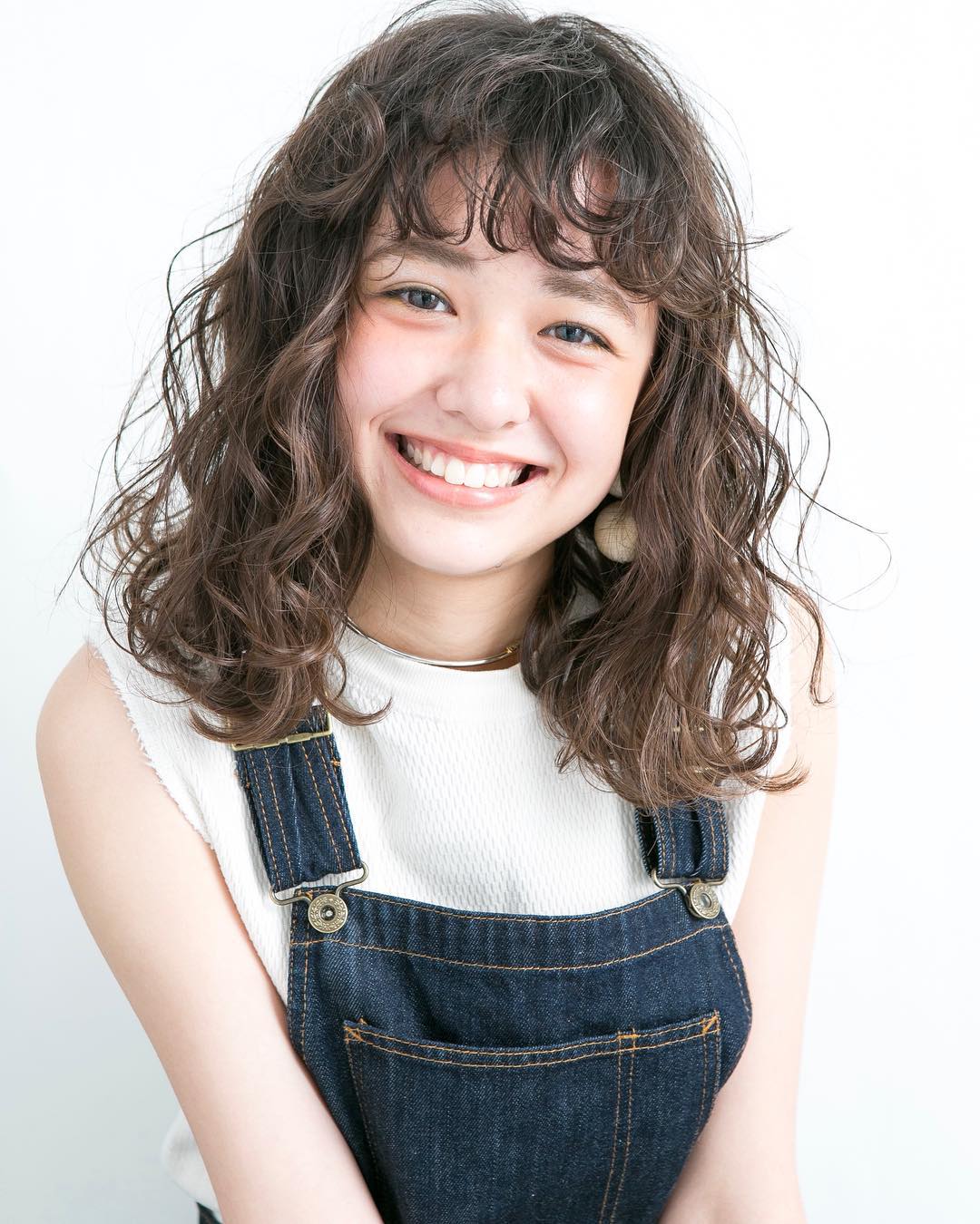 medium length light brown curly perm with bangs.