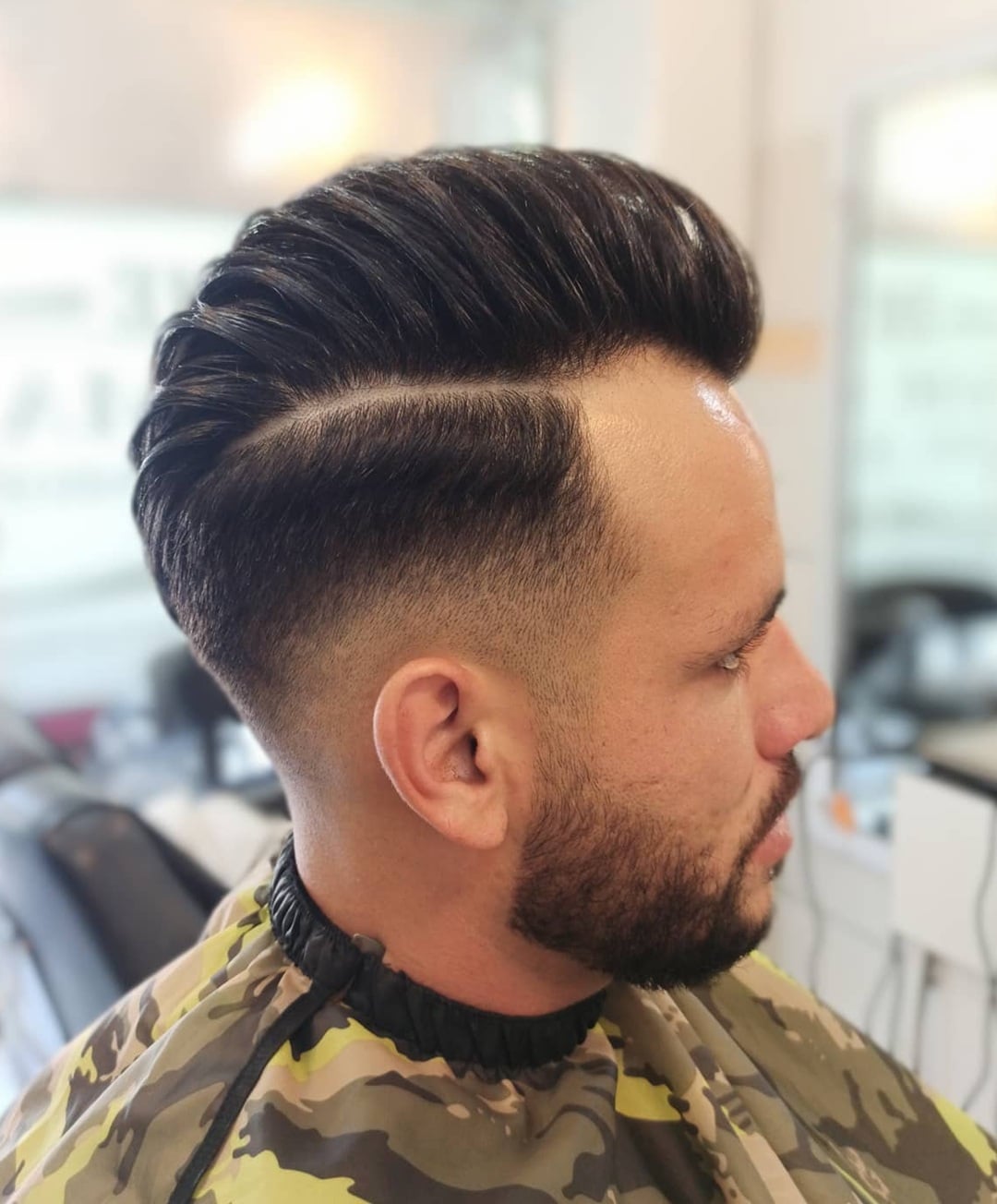 high-volume side part comb over haircut, sharp hard part, clean mid fade, and a trimmed short beard