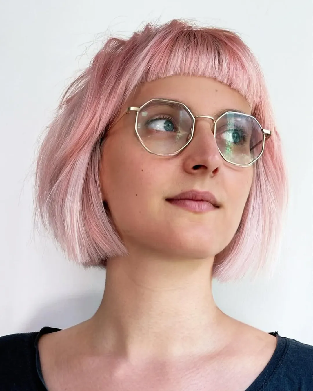 Woman with a pastel pink Dutch boy haircut featuring short blunt bangs